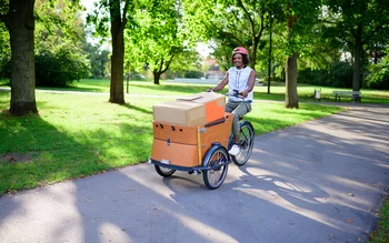 Mann fährt mit Lastenrad mit Kartons im korb durch Park